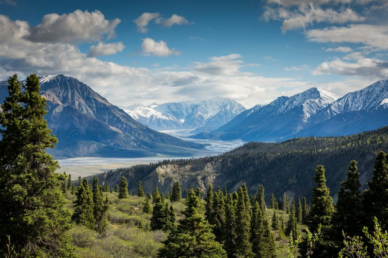 A snowy mountain range above a forested valley and river